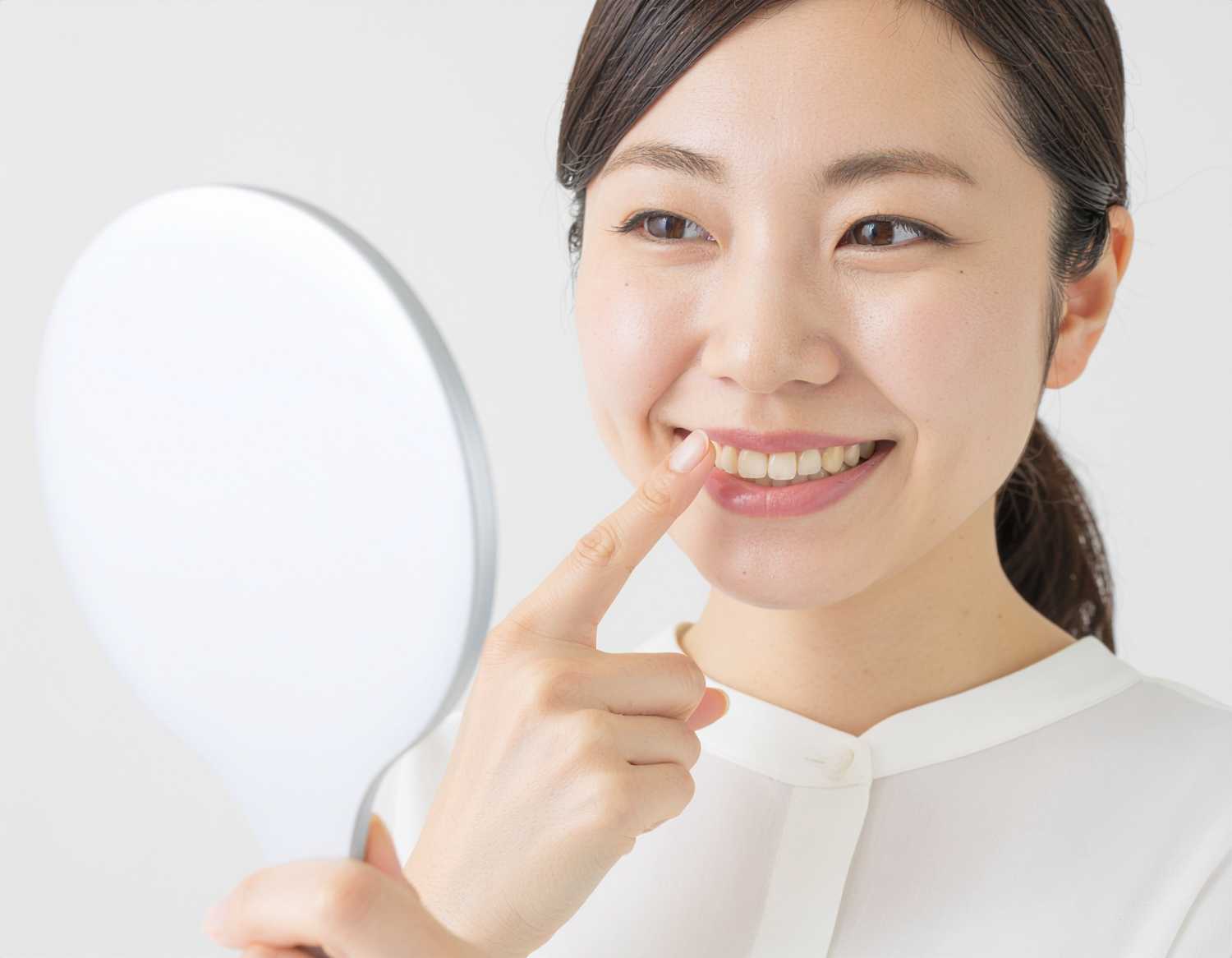 Image 4 Ultraで「手持ち鏡で自分の顔を見る20代の日本人女性。笑顔で白い歯が見える。左手の人差し指を口元に向けている。明るいイメージ」というプロンプトで出力した画像